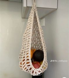 a crocheted bag hanging from a hook with fruit in it and an avocado inside