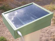 a green and white box sitting on the side of a dirt road next to grass