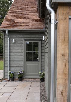 a small gray house with a red roof and brown shingles on the front door