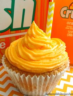 a cupcake with orange frosting and a lit candle on top next to an orange box