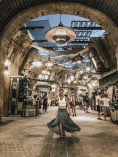 a woman in a long skirt is walking through an old train station with lots of people