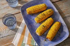 corn on the cob with herbs and salt in a blue plate next to two glasses