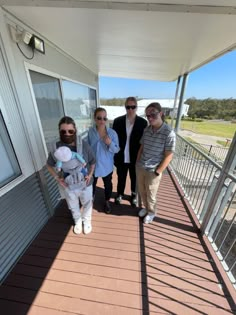 four people standing on a porch with one holding a stuffed animal and the other wearing sunglasses