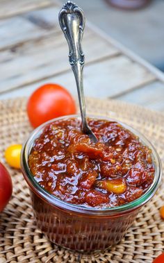 a spoon full of tomato sauce sitting on top of a table next to some tomatoes