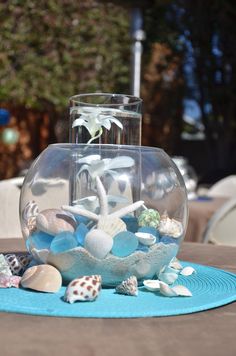 a fish bowl filled with rocks and shells on top of a blue place mat in front of a table