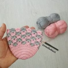 a hand holding a small crochet pot holder next to two balls of yarn