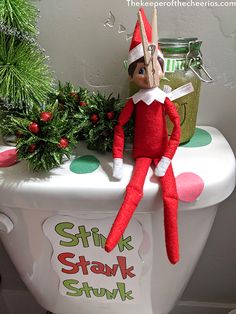 an elf sitting on top of a toilet seat next to a potted plant and christmas decorations