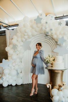 a pregnant woman standing in front of a cake with stars and balloons on the wall