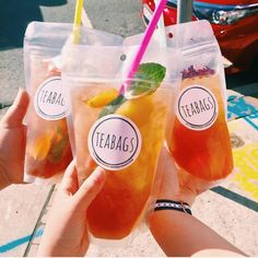 three people holding up drinks in plastic bags with straws and lemon slices on them