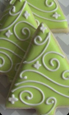 two green decorated cookies with white swirls on them