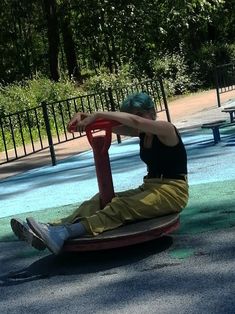 a young man sitting on top of a red object in a park next to a playground