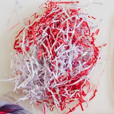 red, white and purple shredded paper on top of a cutting board with scissors next to it