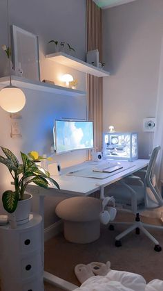 a white desk with a monitor and keyboard on it in front of a window next to a potted plant