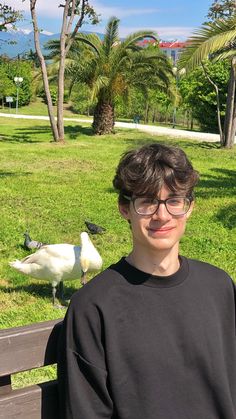 a young man sitting on a bench next to a white bird