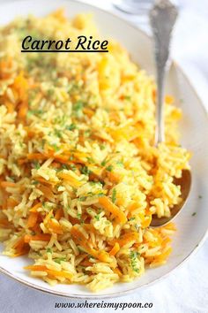 a white plate topped with rice and carrots next to a silver spoon on top of a table