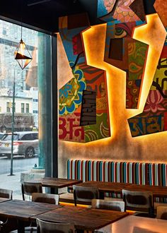 the interior of a restaurant with colorful artwork on the wall and wooden tables in front of it