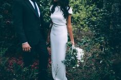 a man and woman in formal wear standing next to each other with flowers on the ground