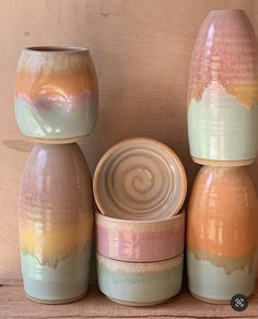 three ceramic vases sitting next to each other on a wooden shelf, one has a lid