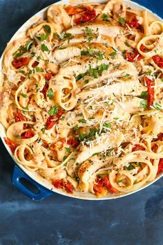 pasta with chicken, tomatoes and parmesan cheese in a skillet on a blue surface