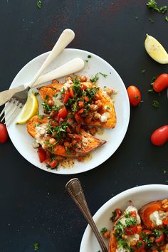 two white plates topped with food next to lemon wedges and tomatoes on a table