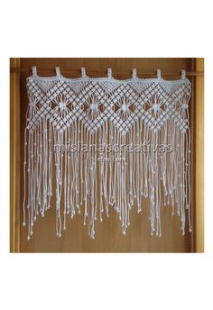 white crocheted curtain with fringes hanging from the side on a wooden wall