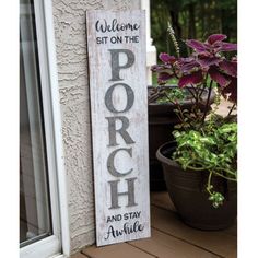 a wooden sign that says welcome sit on the porch and stay awhile next to potted plants