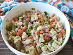 a white bowl filled with shrimp salad on top of a wooden table next to a colorful towel