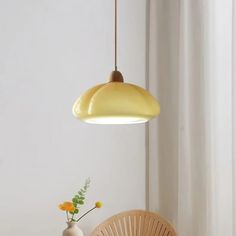 a yellow light hanging over a table with a vase and flowers on it next to a wicker chair