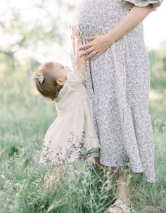 a pregnant woman holding her baby's hand while standing in tall grass