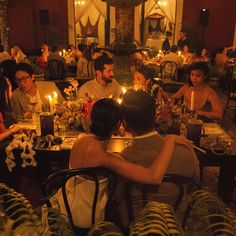 a group of people sitting around a dinner table with candles in the middle of them