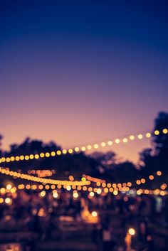 many people are gathered together at an outdoor event with lights strung across the night sky