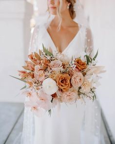 a bride holding a bouquet of peach and white flowers on her wedding day at the beach