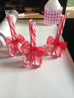 three candy canes tied together with red bows on a white counter top next to a bottle