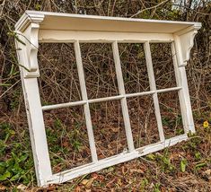 an old window sitting in the middle of a field next to some bushes and trees