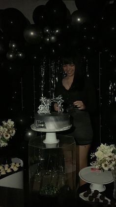 a woman standing in front of a cake on top of a table with black balloons