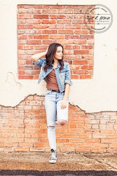 a woman leaning against a brick wall with her hand on her head and looking off to the side