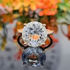 an oval cut diamond sits on top of two wedding rings in front of colorful flowers