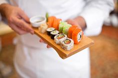 a person holding a wooden tray with sushi on it