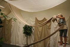 a woman standing in front of a white drape covered wall next to a potted plant