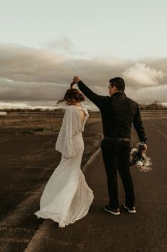 a bride and groom walking down an empty road in the middle of their wedding day