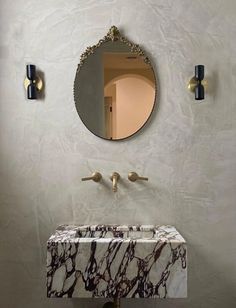 a bathroom sink with a marble counter top and gold faucet, in front of a round mirror