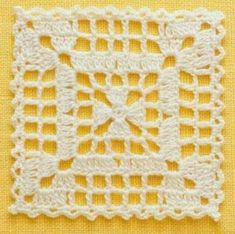 a white crocheted square on top of a yellow table cloth with an intricate design