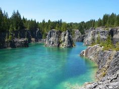 the blue water is surrounded by large rocks and pine trees on either side of it