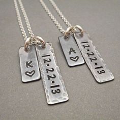 two silver necklaces with names and hearts hanging from the same chain on a gray surface