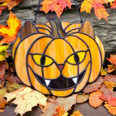 a pumpkin with a cat's face painted on it sitting in the fall leaves