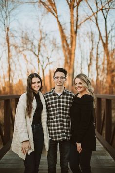 three people standing on a bridge in front of trees