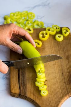 a person cutting green peppers with a knife on a cutting board next to other cut up vegetables