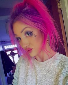 a woman with pink hair and piercings on her face is looking at the camera