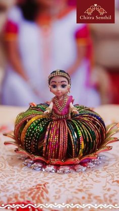 a small doll sitting on top of a colorful object in the middle of a table