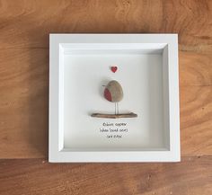 a white frame with a small bird in it on a wooden table next to a red heart